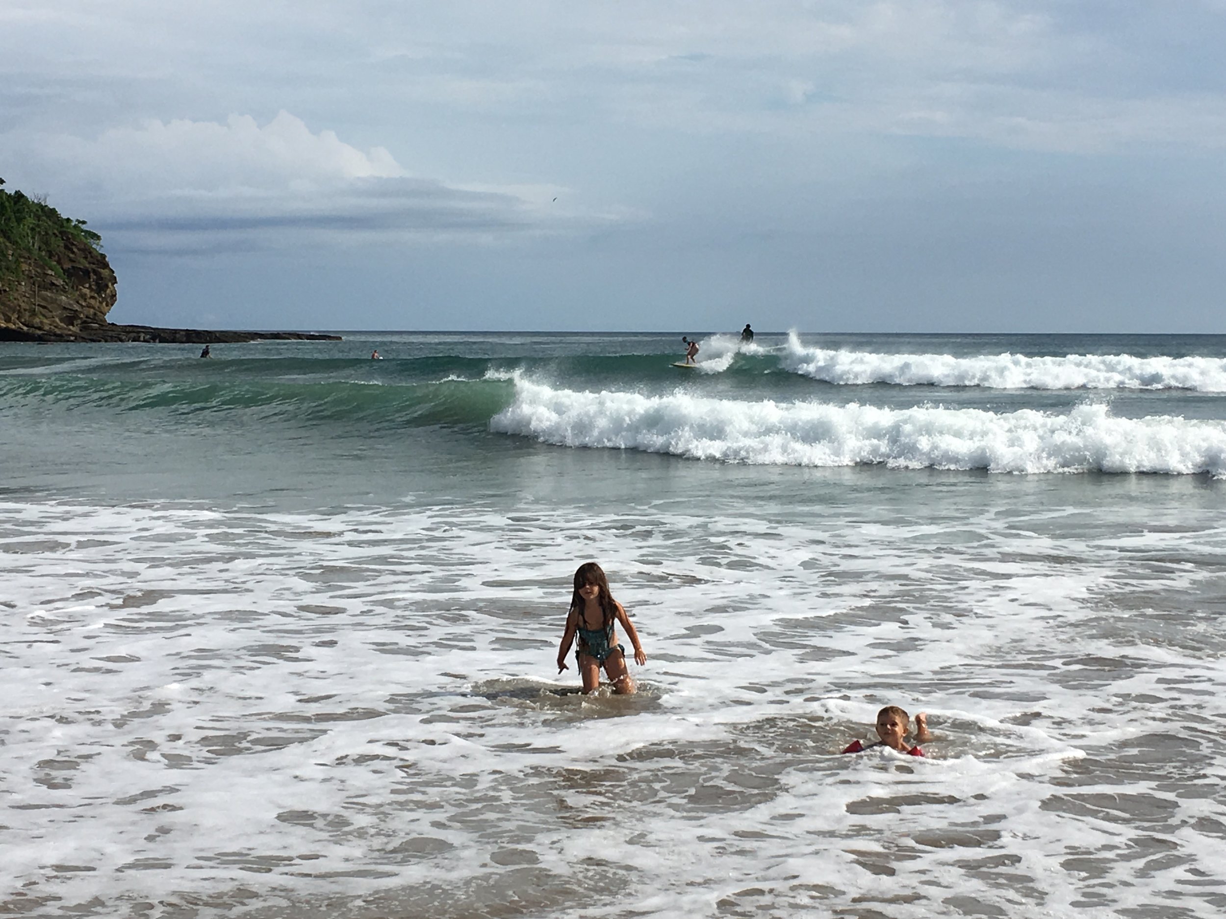  Surfers catching waves and children wading close to shore 